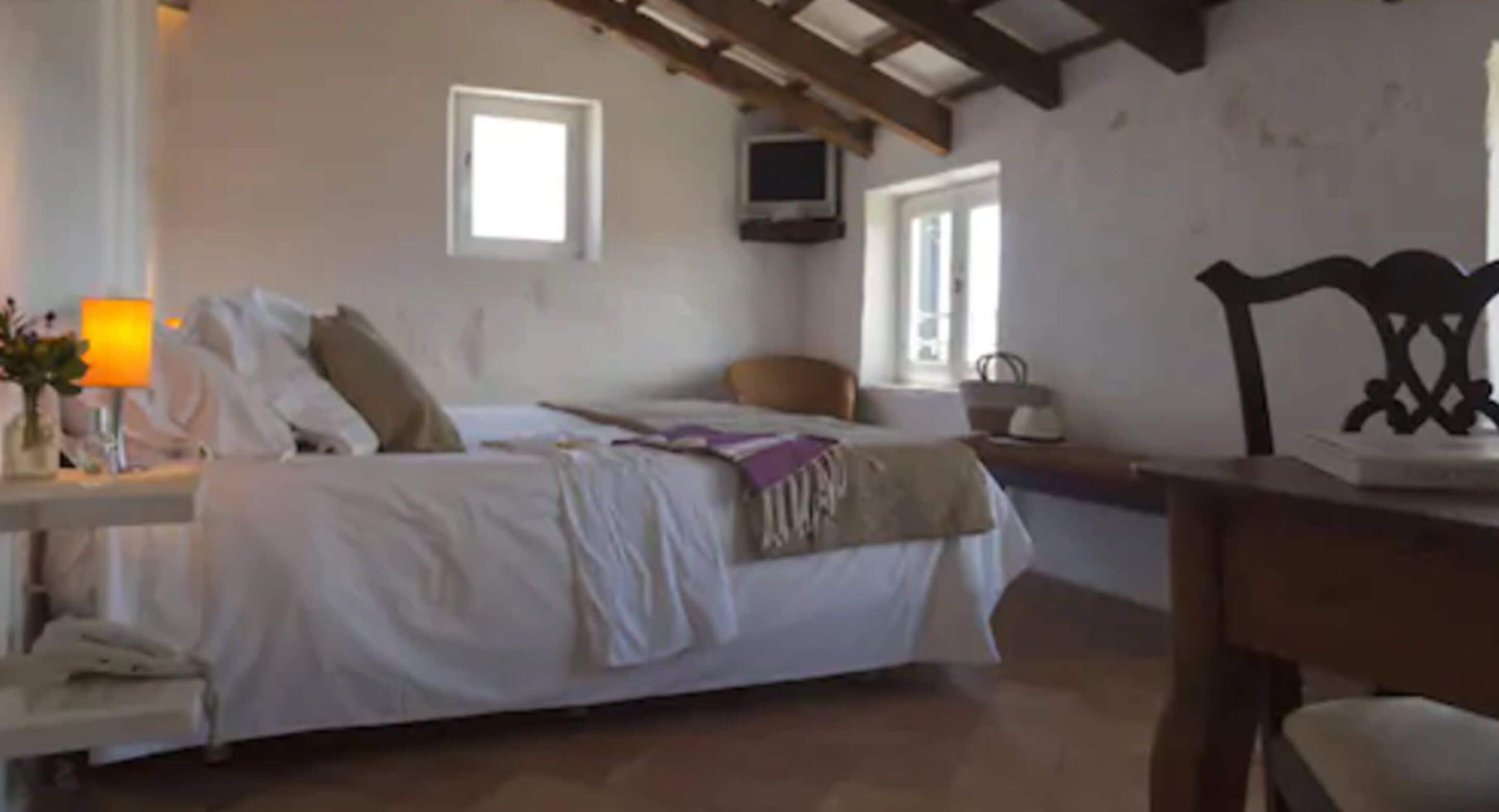 A bedroom with a bed, bedside table, lamp, and a window.