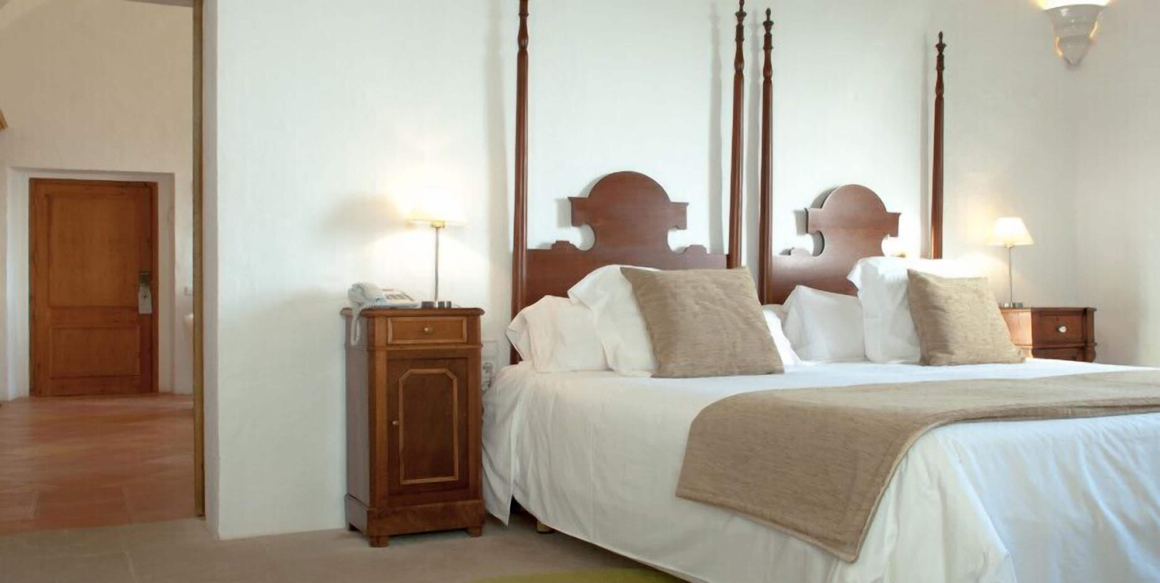 A bedroom with a four-poster bed, a nightstand with a lamp, and a wooden wardrobe.
