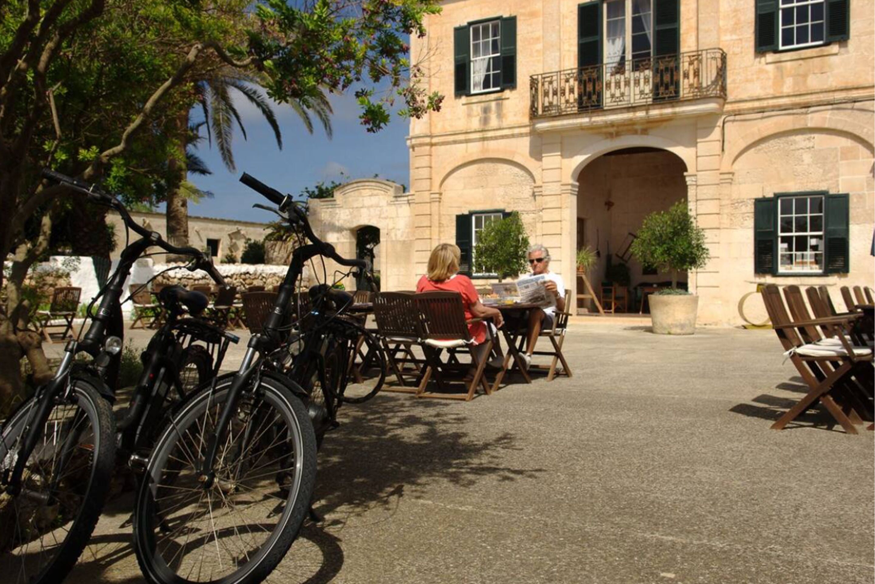 Un patio con bicicletas, mobiliario exterior y un edificio con arcos y balcones.