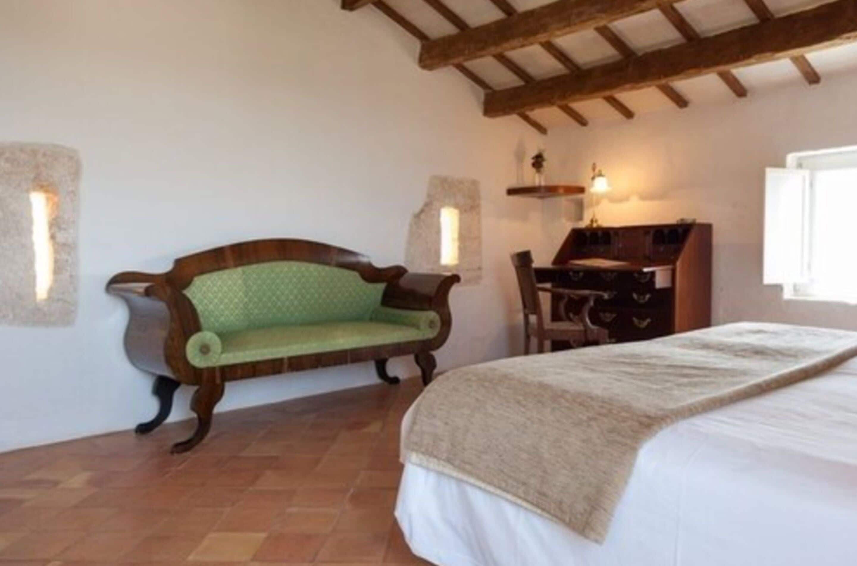 A bedroom with a bed, a wooden bench, a desk, and a chair.