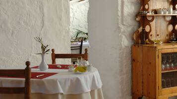 Uma área de refeições com uma mesa posta para dois, um armário de madeira com copos e um muro branco com textura.