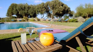 A poolside setting with a lounge chair, a table with a glass of water, a bottle, and a yellow vase. -  Alcaufar Vell Hotel Rural & Restaurant (Sant Lluis)