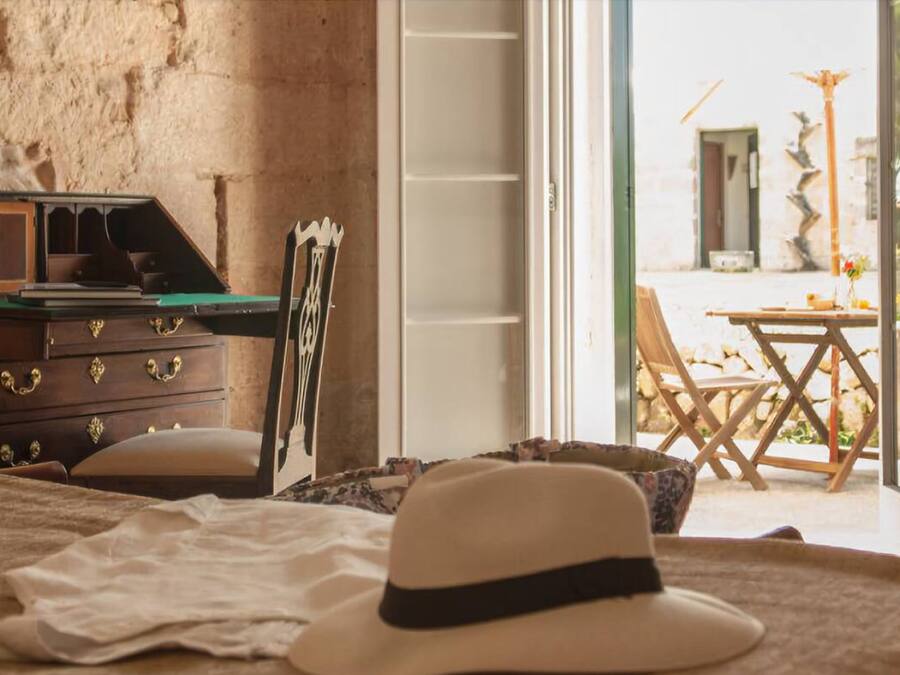 A bedroom with a bed, a dresser, a hat, and a view of an outdoor patio with a table and chairs.