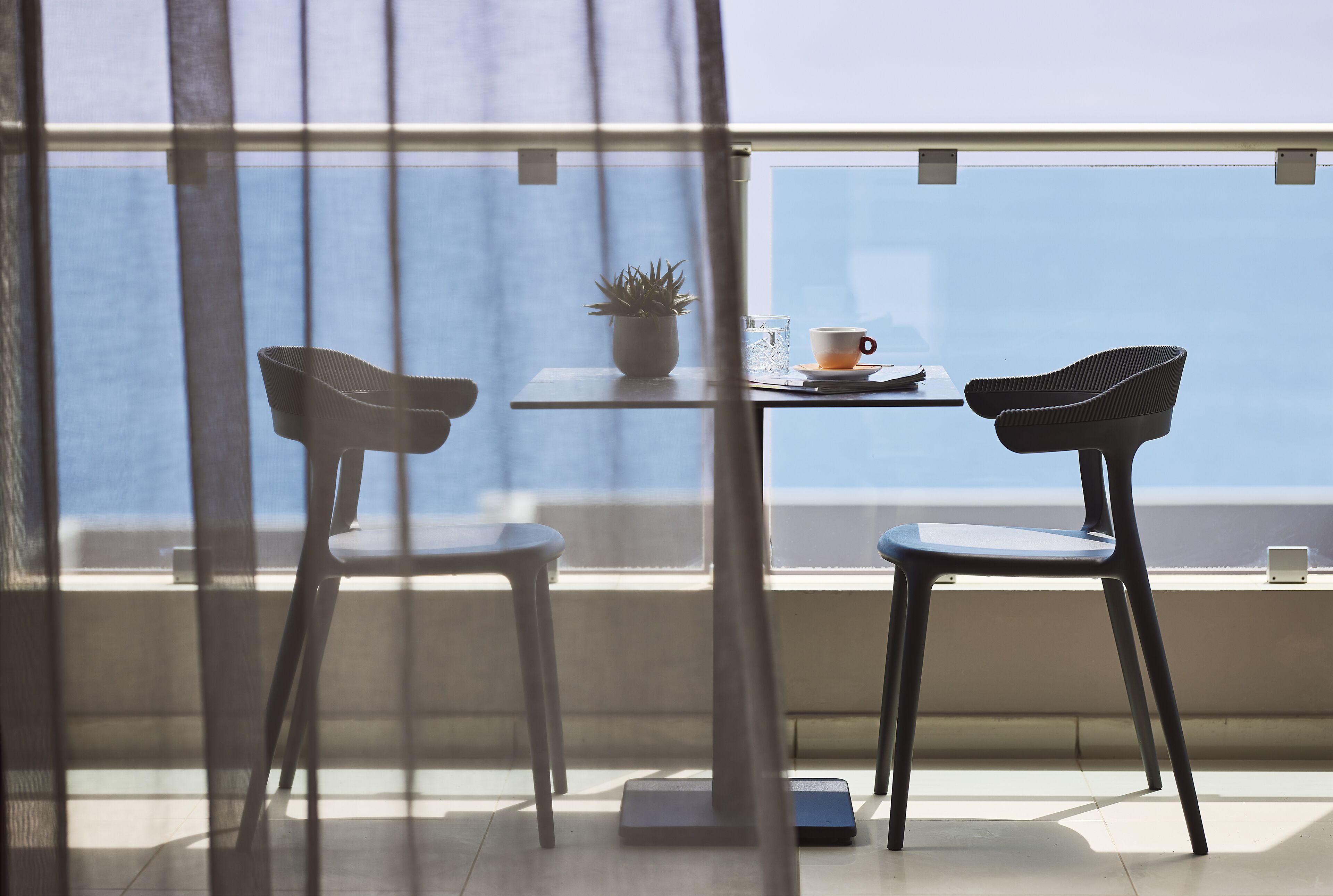 A balcony with two chairs, a small table, a potted plant, and a cup.