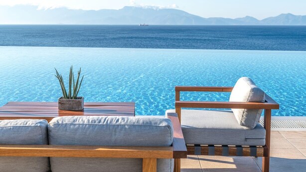 En infinitypool med en träbänk och en bekväm fåtölj, placerade så att man har utsikt över bergen.