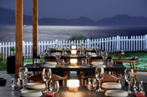 A table set for dining with wine glasses and plates, overlooking a body of water and a white fence. - Michelangelo Resort and Spa (Kos)