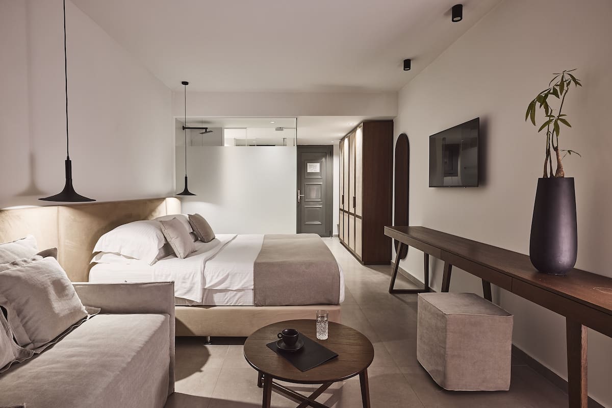 A modern hotel room with a bed, a sofa, a small table with a cup and a glass, and a potted plant.
