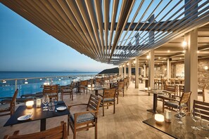 An outdoor dining area with tables and chairs, overlooking a body of water. - Michelangelo Resort and Spa (Kos)