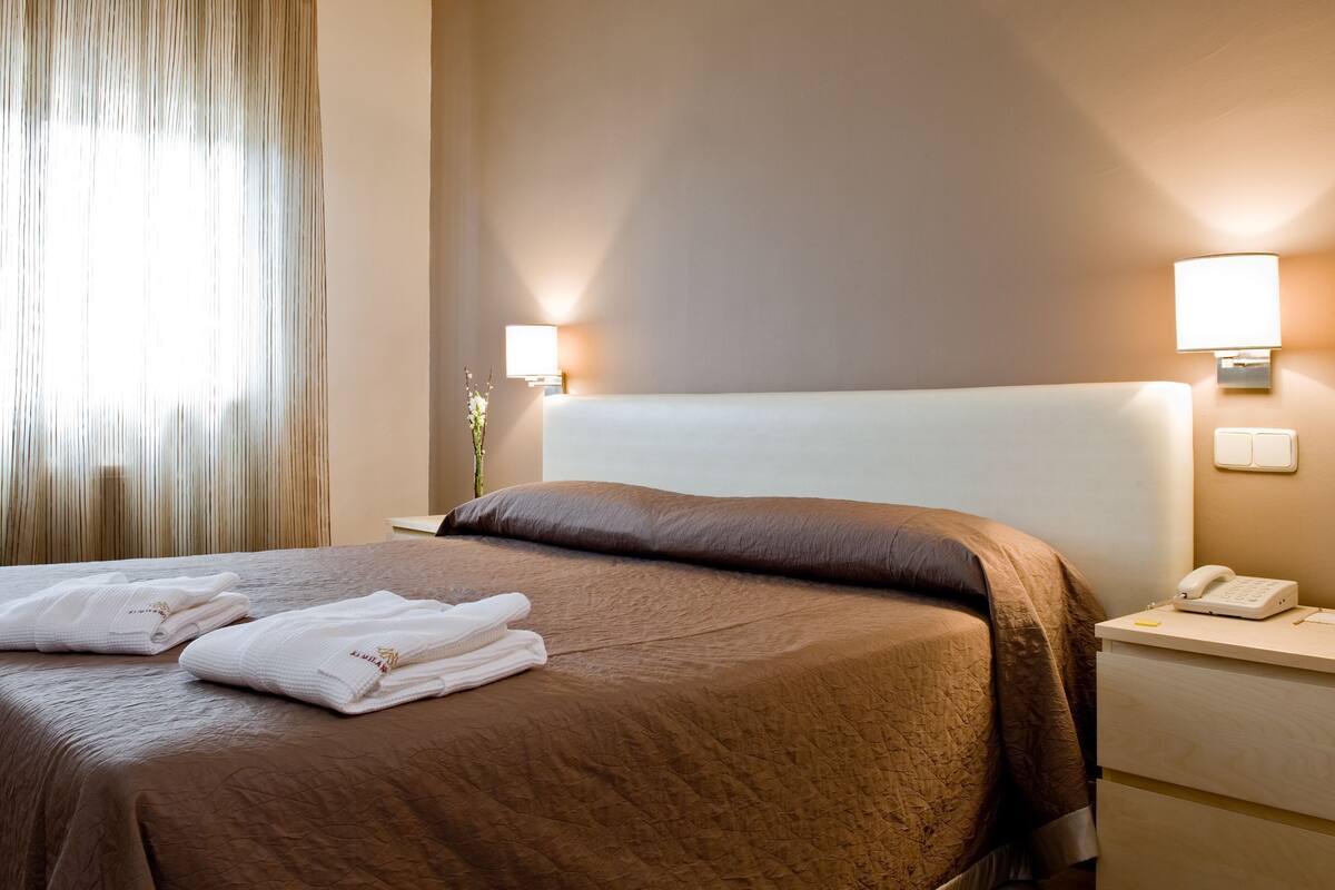Una habitación de hotel con una cama, dos lámparas de noche, un teléfono y una mesita de noche.