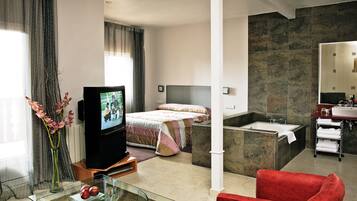 Habitación de hotel con cama, televisor, una mesita de vidrio con una manzana, una silla roja y un baño con bañera y lavamanos.