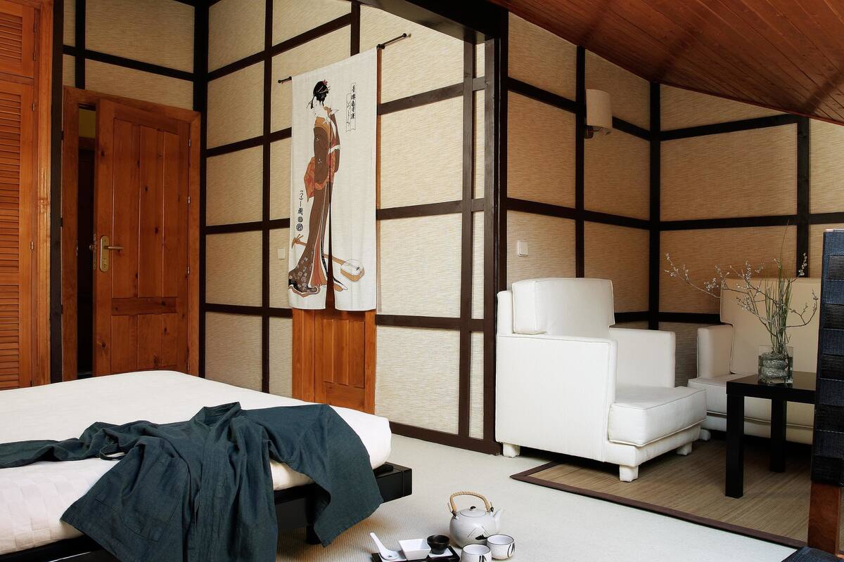 Una habitación tradicional japonesa con suelo de tatami, cama baja, sofá blanco y un juego de té sobre el suelo.