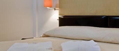 A neatly made bed with two folded towels, a headboard, and a wall-mounted lamp.