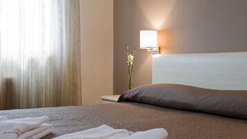 A neatly made bed with a brown headboard, a bedside lamp, and folded towels on a wooden nightstand.