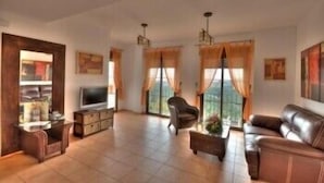 A spacious living room with a flat-screen TV, leather sofas, and a large window with curtains. - Apartamentos Bahía Santa Cruz (Almunecar)