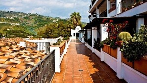 A corridor with terracotta tiles, white walls, and balconies with potted plants. - Apartamentos Bahía Santa Cruz (Almunecar)