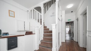 Un vestíbulo de hotel moderno y luminoso con un mostrador de recepción de madera, una escalera con barandillas blancas y un cartel con los números de las habitaciones.
