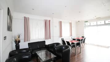 A modern hotel lobby with leather seating, a glass coffee table, and a dining area with red tables and chairs.