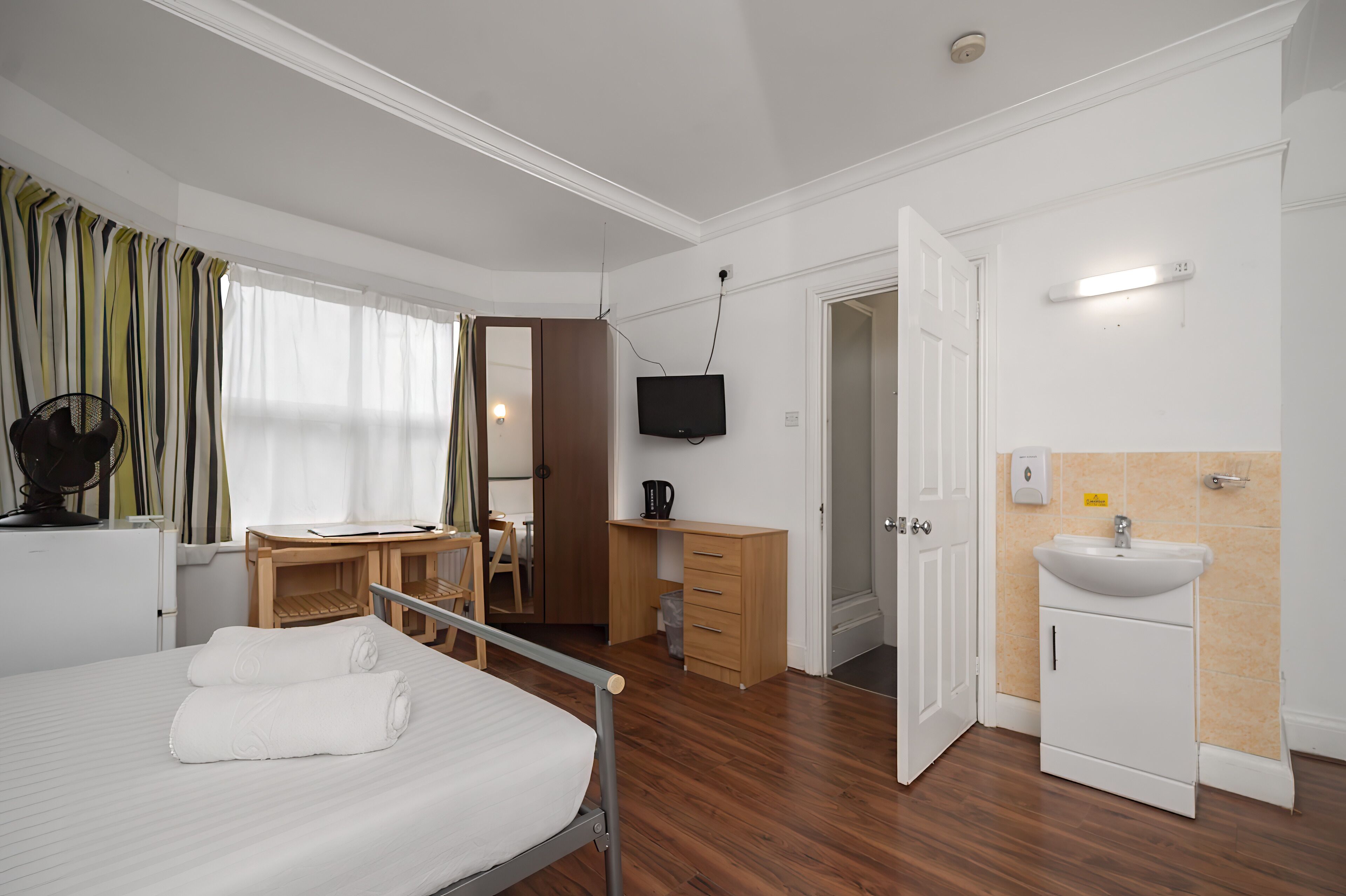 Camera d'albergo con un letto, una scrivania, una televisione, un armadio e un bagno con un lavandino.