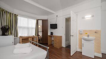Camera d'albergo con un letto, una scrivania, una televisione, un armadio e un bagno con un lavandino.