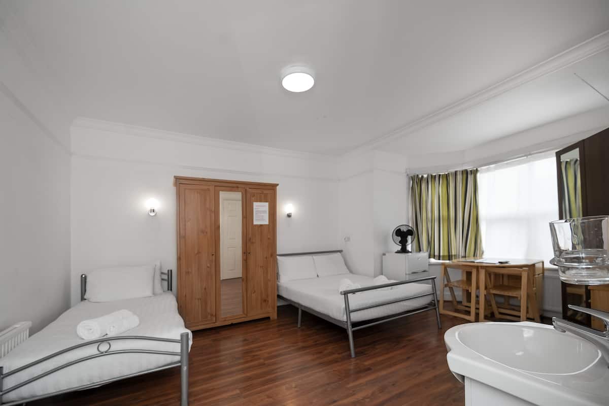 Quarto de hotel com cama, sofá, pequena mesa, cadeira, pia e espelho.