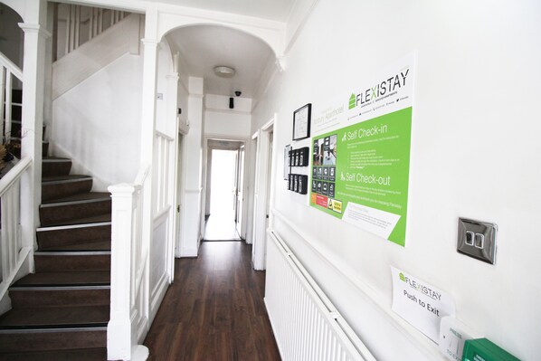 A hotel hallway with a staircase, a self-check-in/out sign, and a push-to-exit sign.