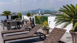 Una terraza en la azotea con sillones de descanso, plantas en macetas y vistas panorámicas de la ciudad.