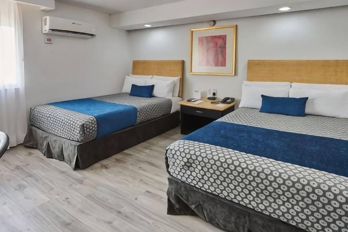 Una habitación de hotel con dos camas, una mesita de noche, un teléfono y un cuadro en la pared.