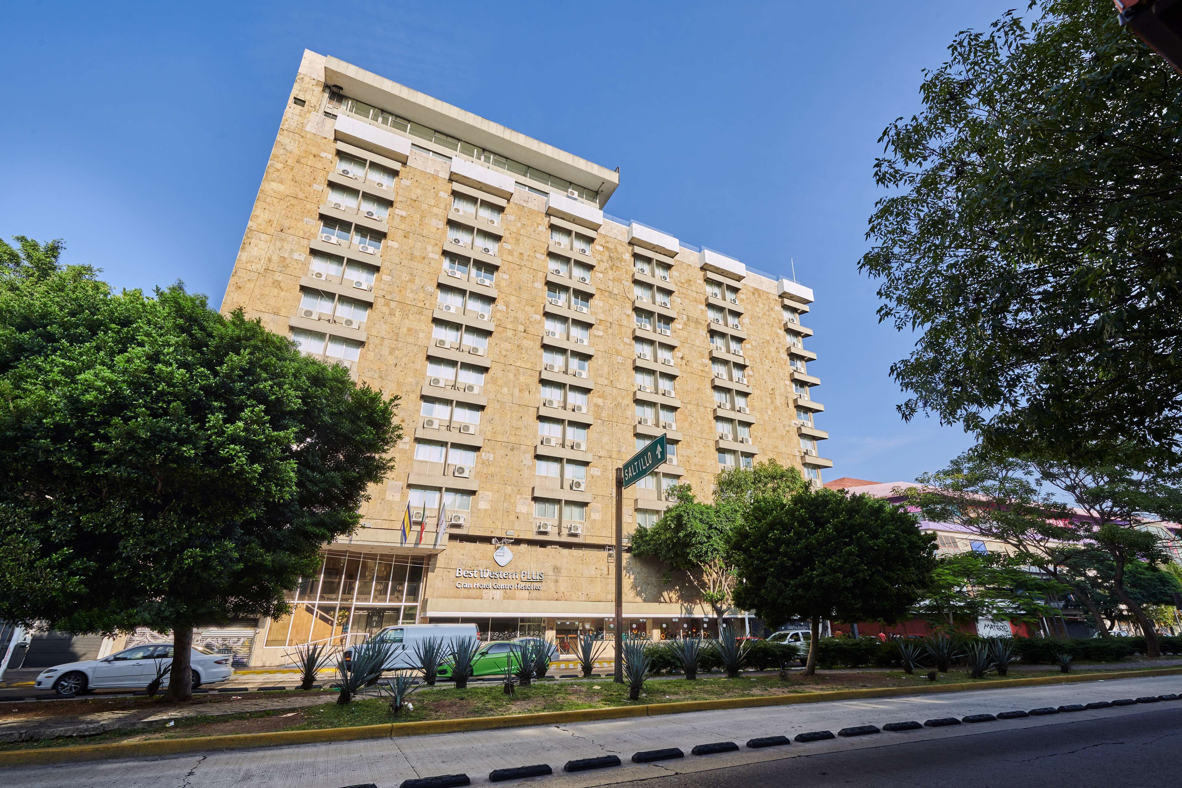Un hotel alto y beige de varios pisos, con entrada central y unidades de aire acondicionado.
