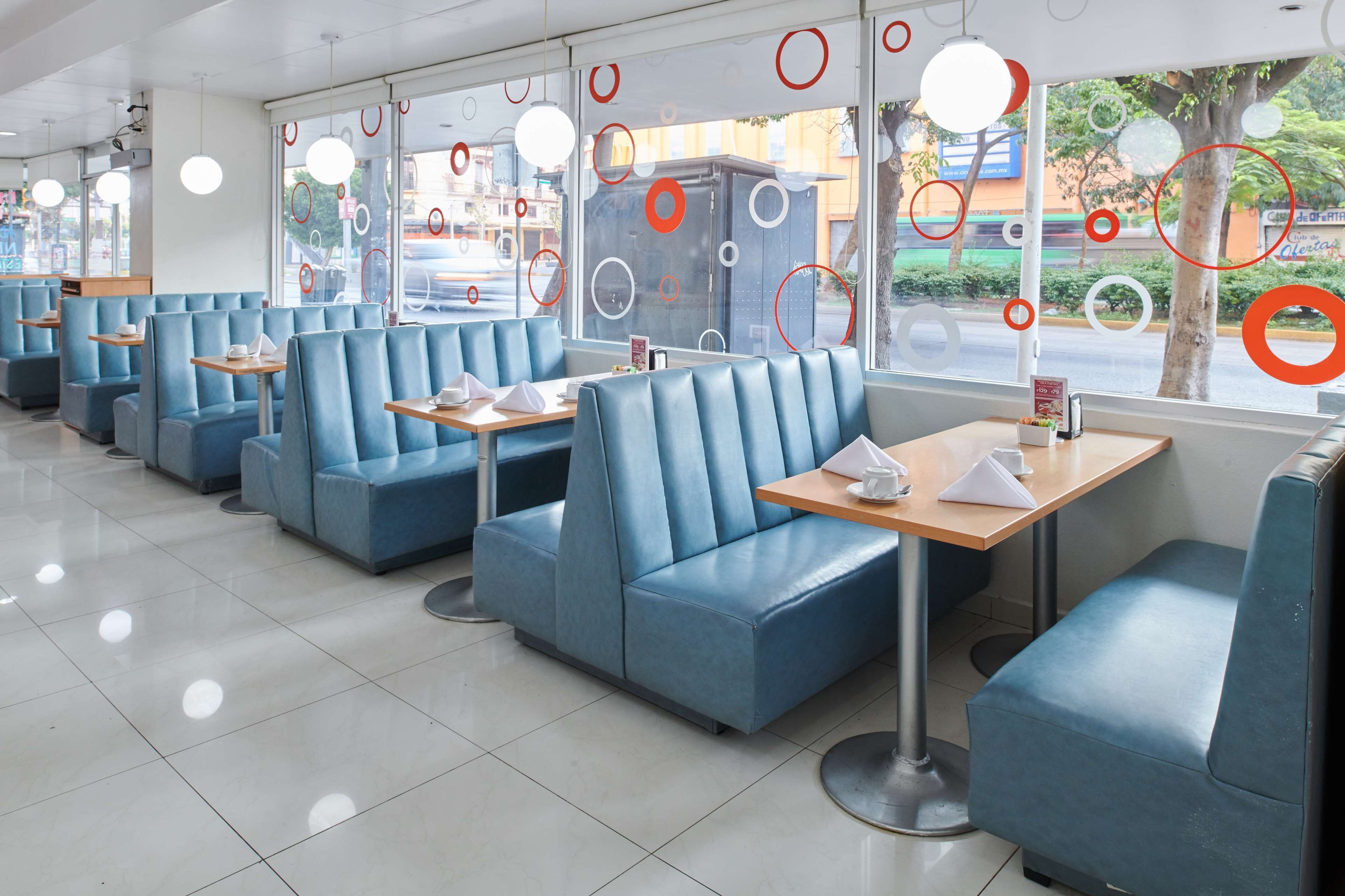 A restaurant with blue booths, round tables, and a view of the street through large windows.