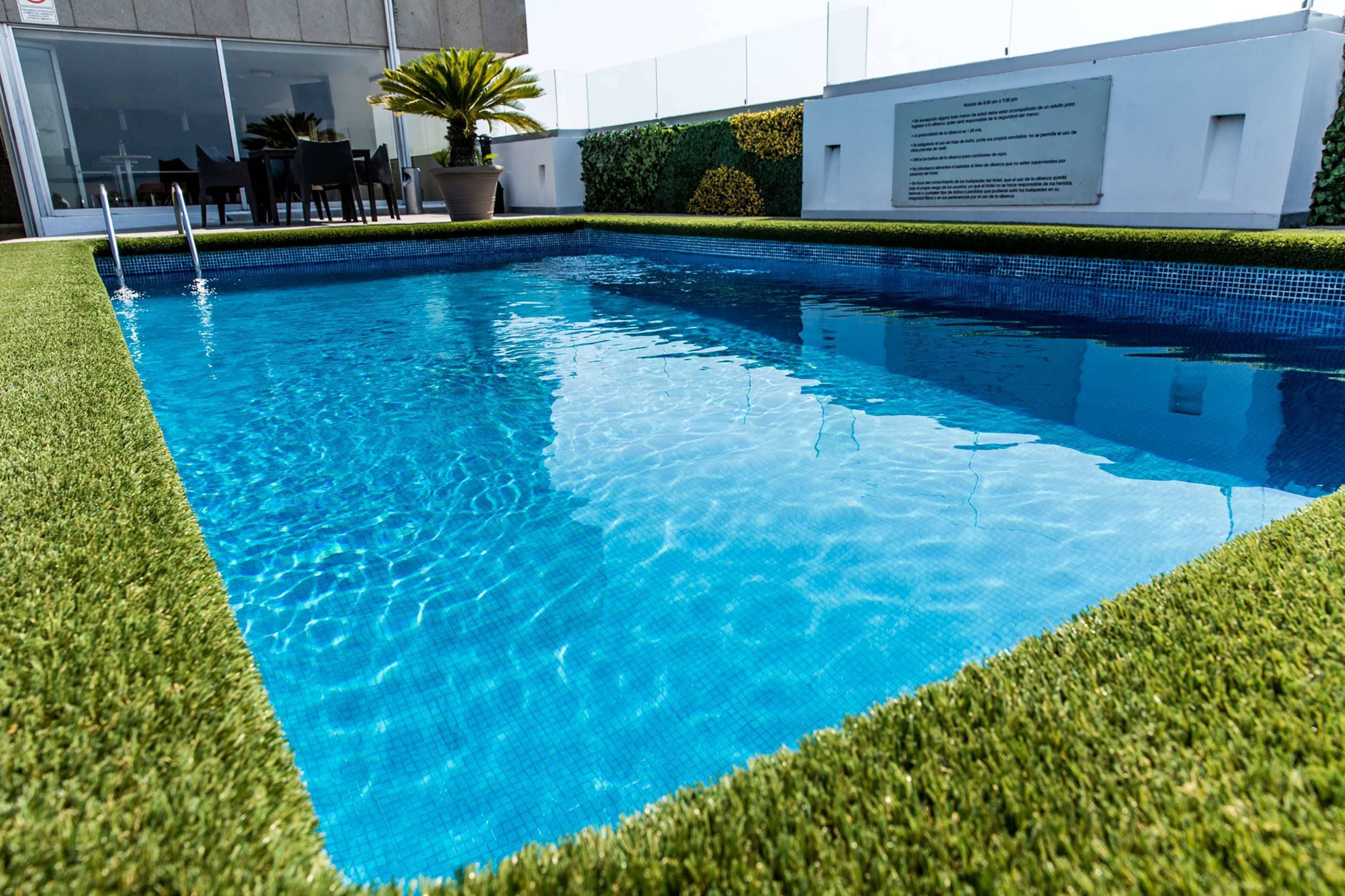 A swimming pool with clear blue water, surrounded by artificial grass and a white building with a sign.