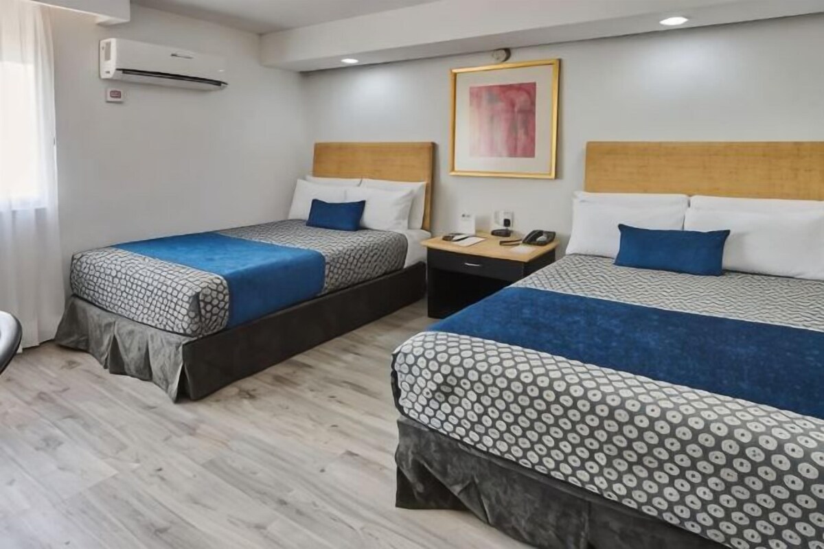 Een hotelkamer met twee bedden, een nachtkastje, een telefoon en een schilderij aan de muur.