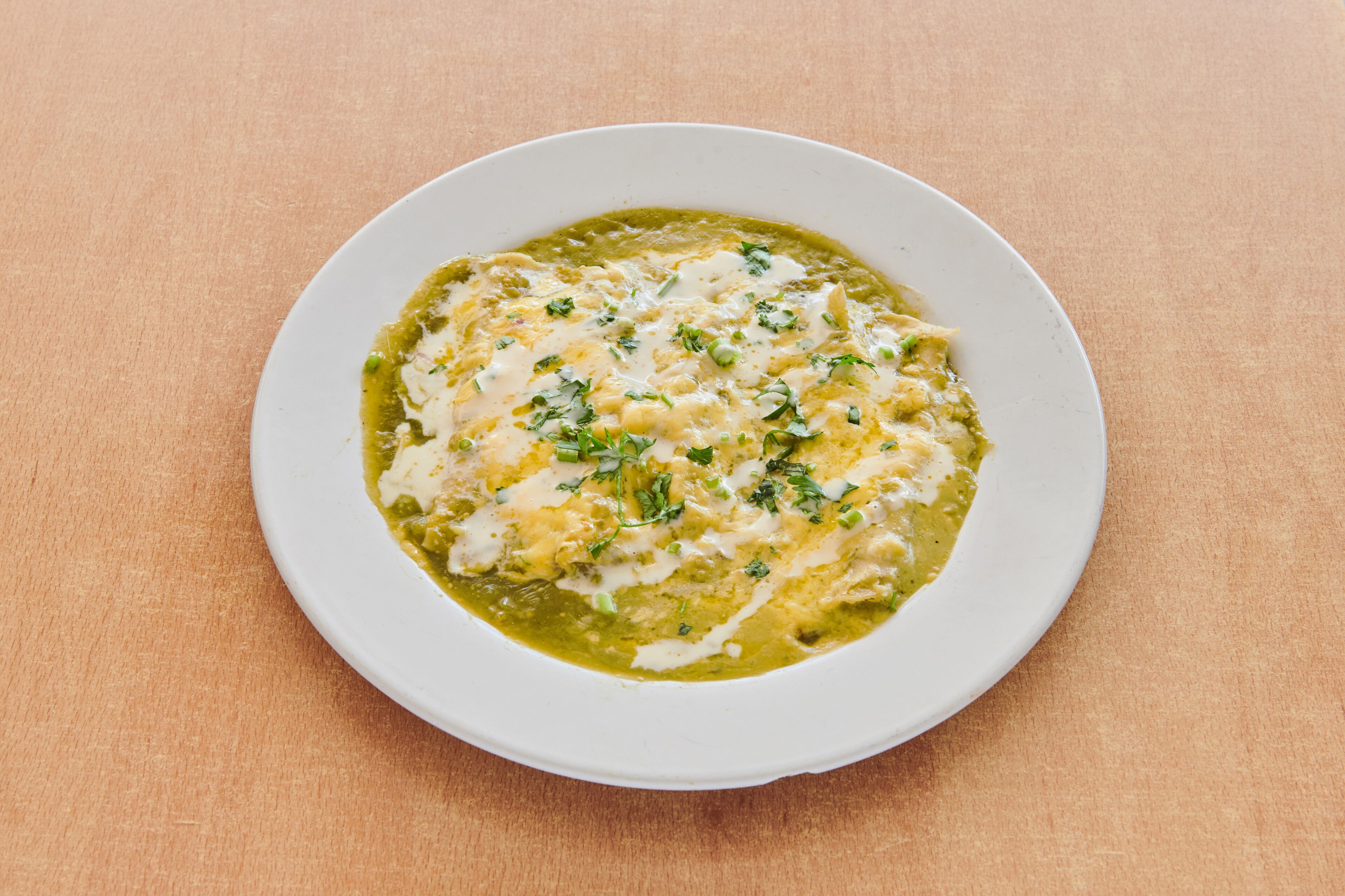A white bowl of green sauce with herbs on a wooden table.
