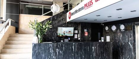Zona de recepción de hotel con mostrador de mármol, una escalera y un cartel que dice "Best Western PLUS Gran Hotel Center".