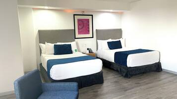 Habitación de hotel con dos camas, una silla y un cuadro en la pared.