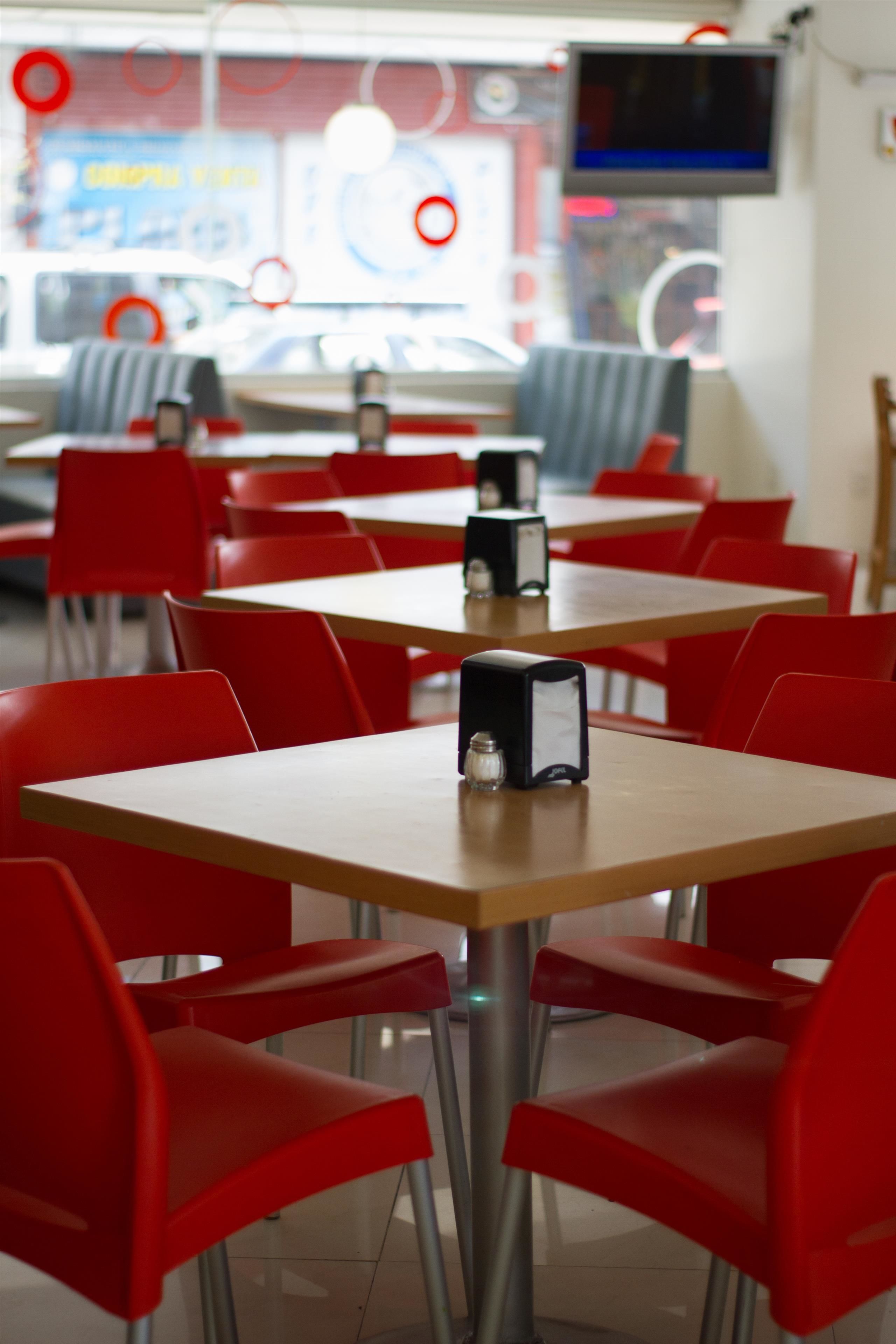 Un comedor con sillas y mesas rojas, un televisor montado en la pared y un ventanal con vistas al exterior.