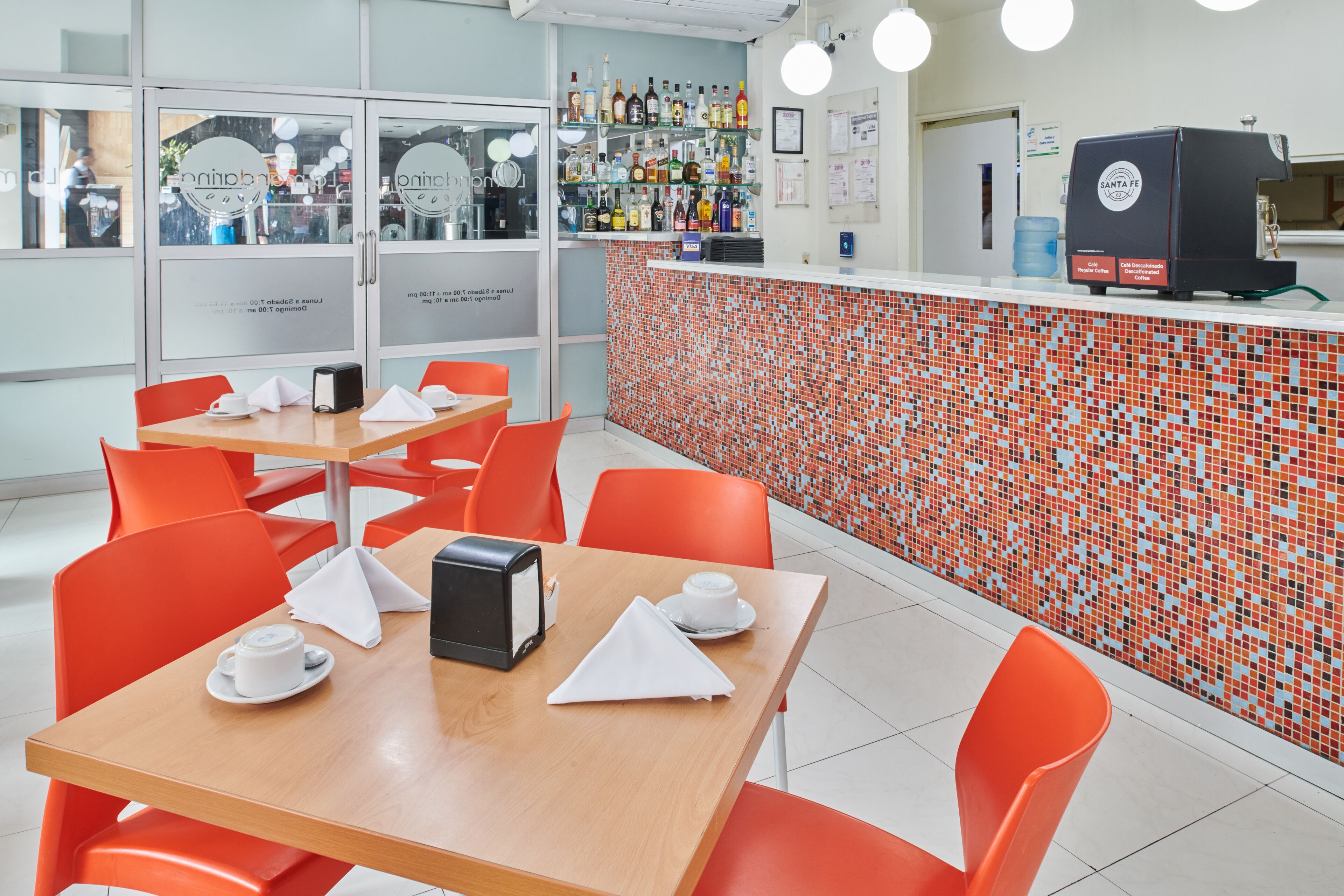 A modern cafe with orange chairs and tables, a tiled backsplash, and a coffee machine.