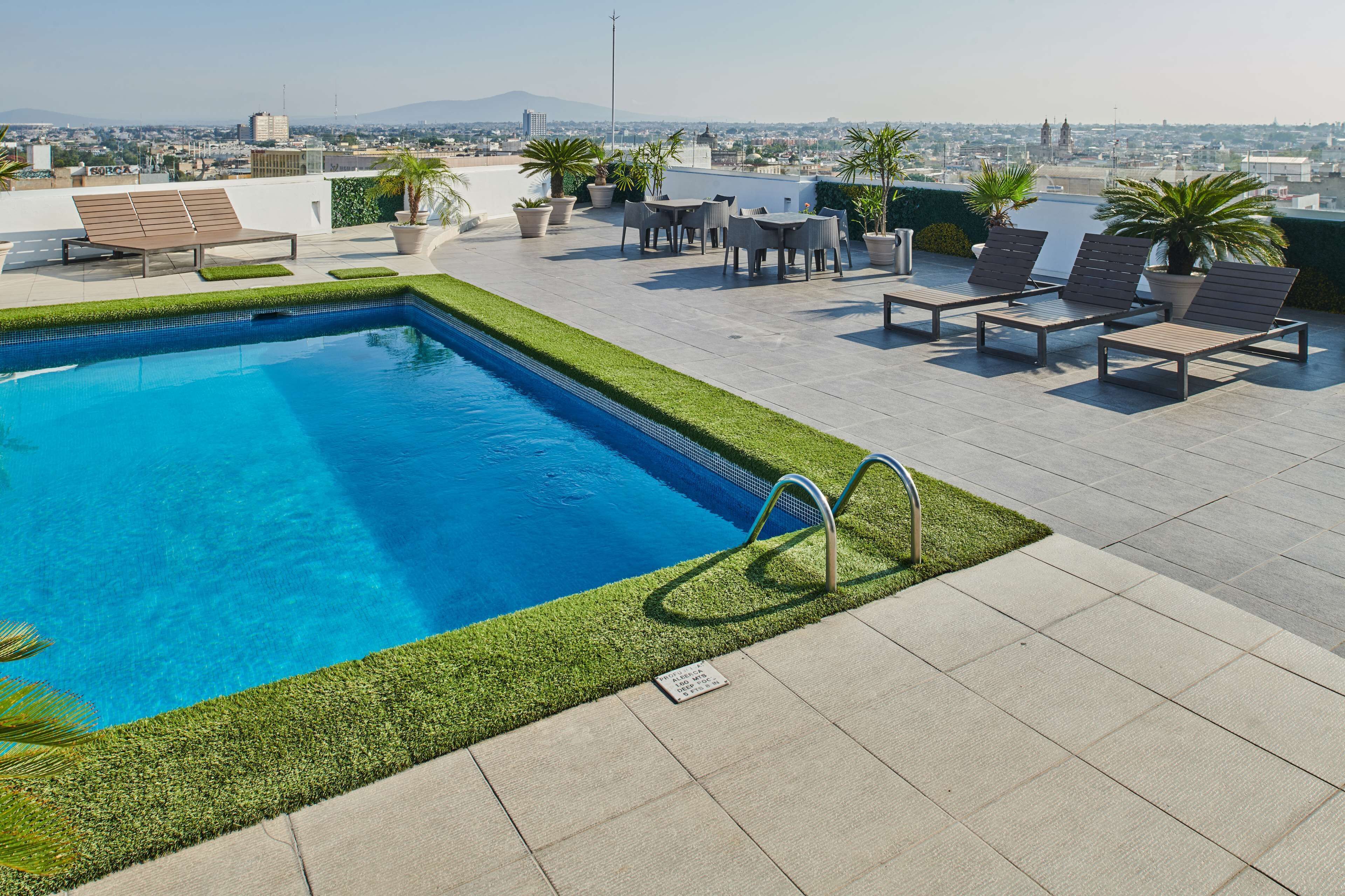 Area piscina sul tetto con vista panoramica sulla città, che include una statua e montagne all'orizzonte.