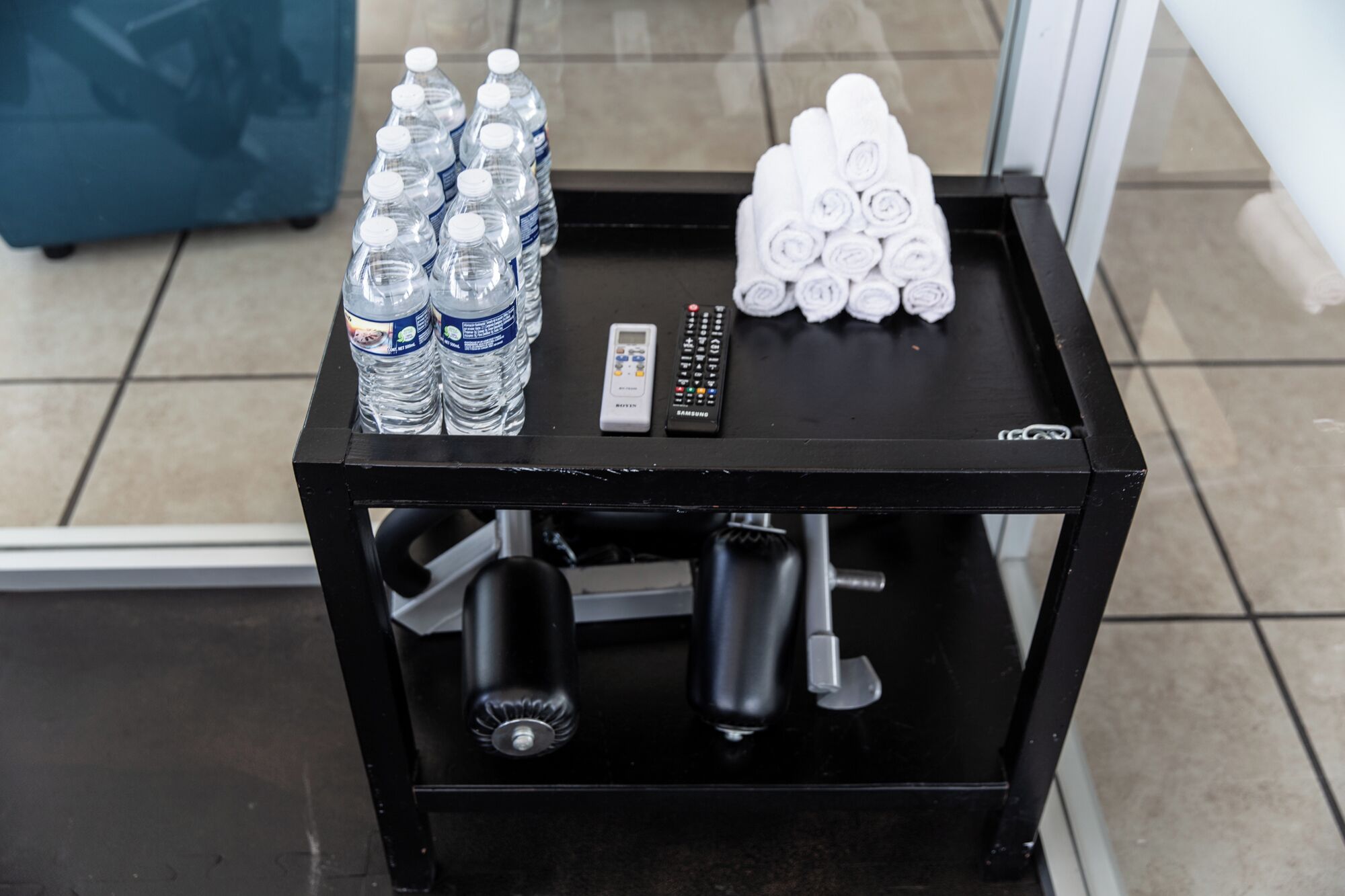 A black metal table with bottled water, a remote control, and rolled towels.