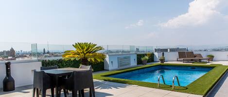 Terraza en la azotea con piscina, zona de estar y vistas a la ciudad.