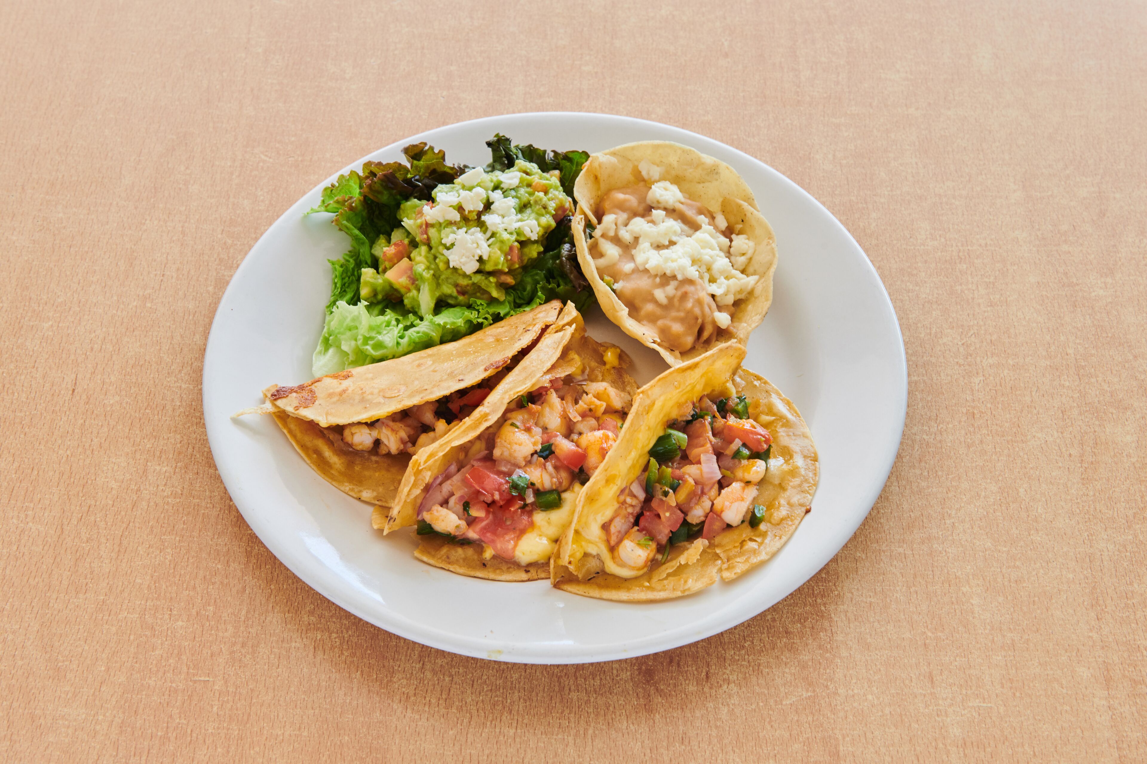 Un plato con tres tacos, una ensalada y un tazón de guacamole.