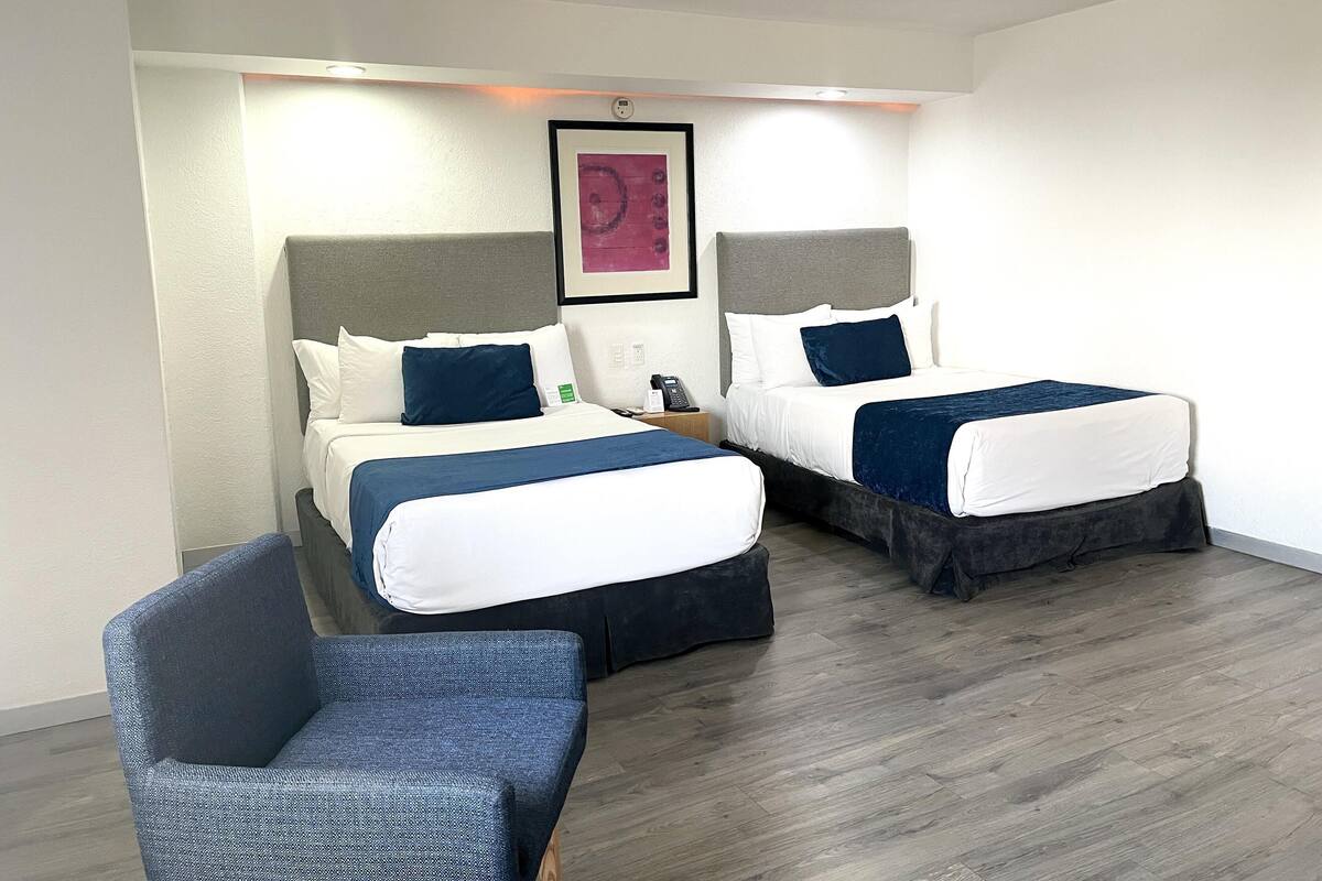 Une chambre d’hôtel avec deux lits, une chaise et un tableau au mur.