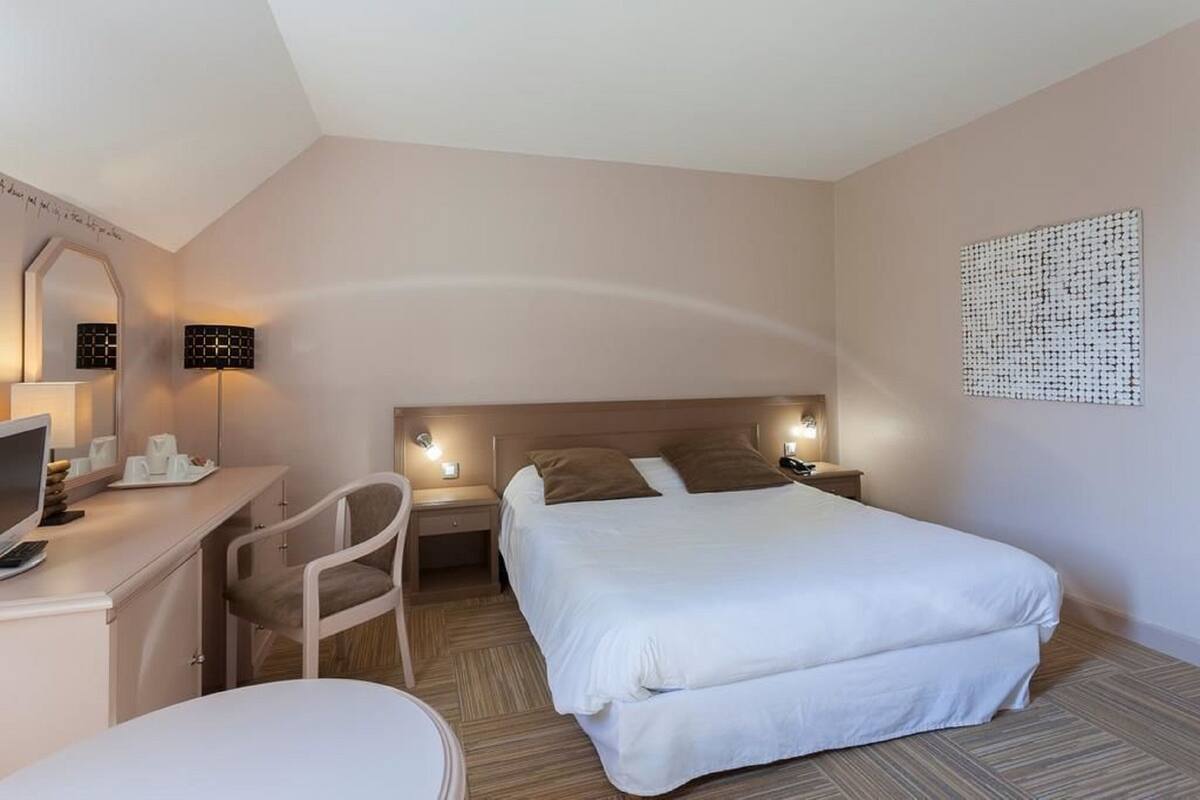 Habitació d'hotel amb llit, escriptori, cadira i làmpades laterals.