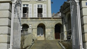 Una entrada con reja y detalles metálicos ornamentales, que conduce a un edificio con múltiples ventanas y fachada de piedra.