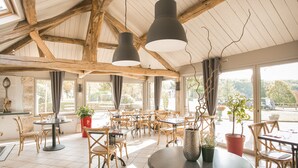 Un comedor amplio con vigas de madera, ventanas grandes y varias mesas y sillas.