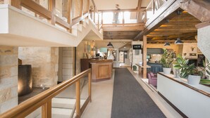 Un interior espacioso con una escalera central, vigas de madera y un mostrador de recepción con plantas.
