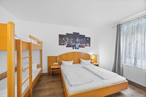 Habitación de hotel con literas, una cama individual, una obra de arte con vista urbana, una mesita de noche y una ventana con cortinas.