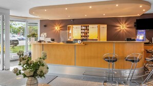 A reception area with a wooden counter, bar stools, a TV, and a Sun Park display. - Sun Parc Hotel (Ringsheim)