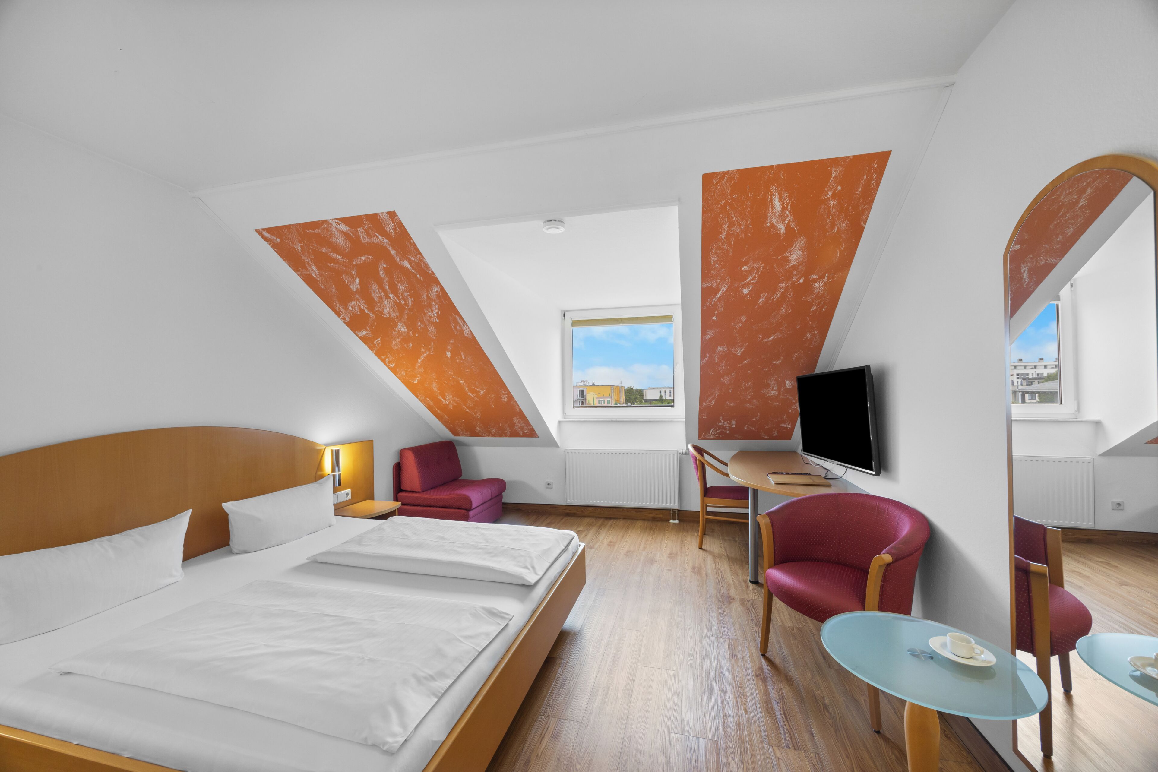 A hotel room with a bed, a desk, a TV, and a chair.