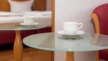 A hotel room with a bed, a red armchair, and two glass-top tables with white cups.