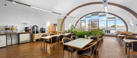 Un'area pranzo moderna con tavoli e sedie in legno, un angolo caffè e ampie finestre con vista.
